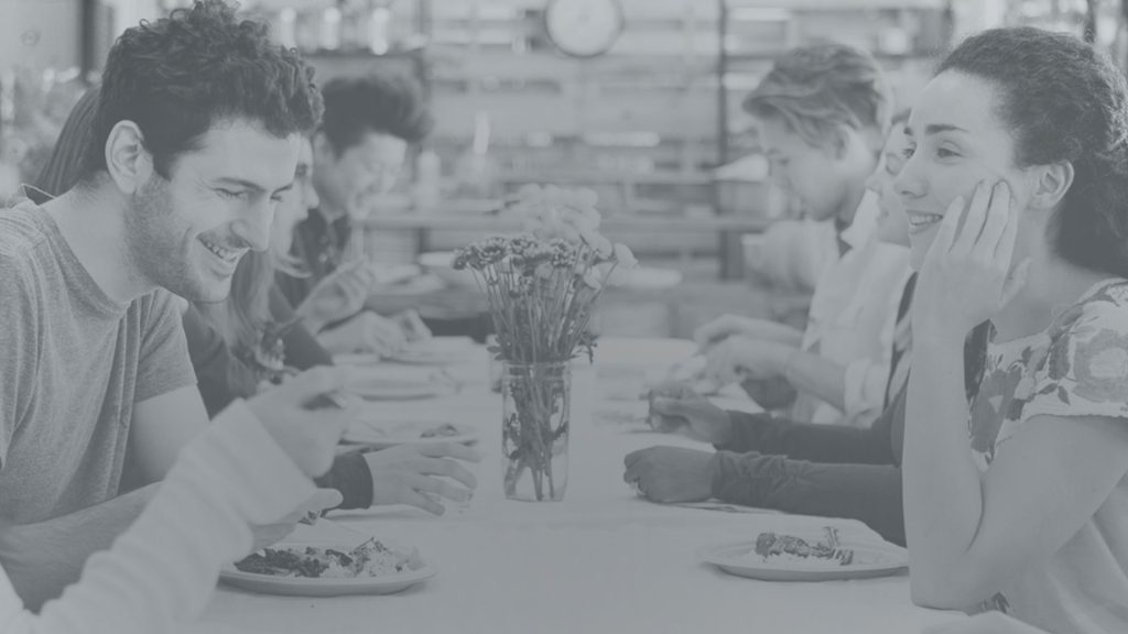 Black-and-white photo of two people smiling and chatting while dining at a restaurant table