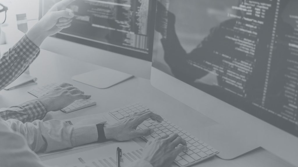 Black-and-white photo of developers working at computers with code displayed on large monitors, representing software development