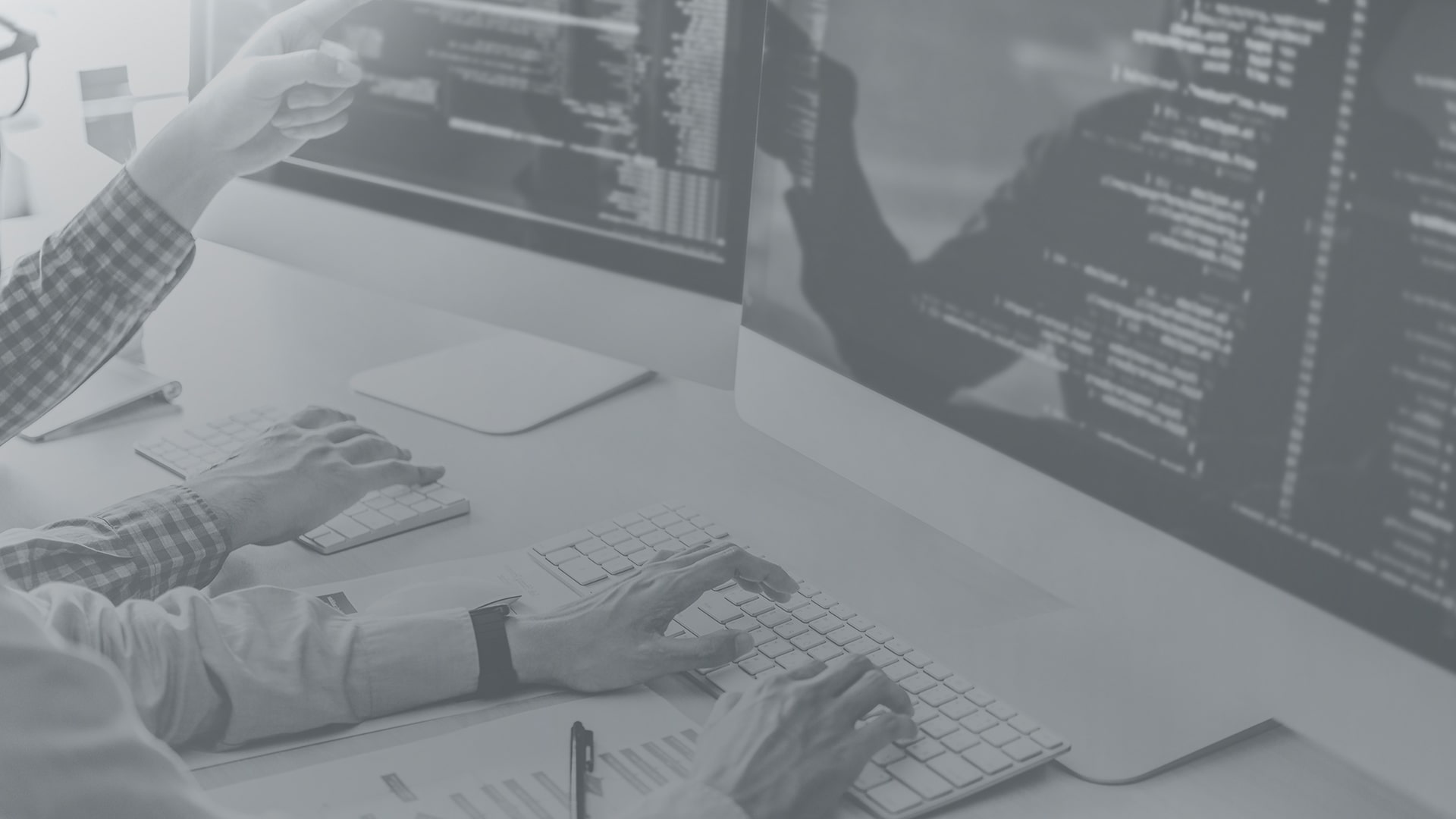 Black-and-white photo of developers working at computers with code displayed on large monitors, representing software development